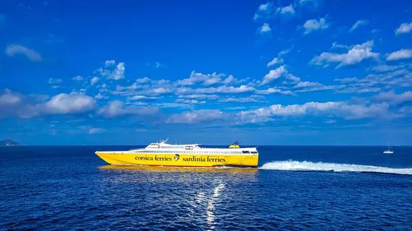 Sarı-beyaz feribot Korsika Sardunya feribotu güneşli bir günde Elba Adası 'na gider. Ön planda koyu mavi bir deniz, arka planda beyaz bulutlu mavi bir gökyüzü. 28 Eylül 2025. Piombino, İtalya.