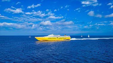 Sarı-beyaz feribot Korsika Sardunya feribotu Elba Adası 'na gidiyor. Önde koyu mavi bir deniz, arkada üç beyaz yelkenli. 28 Eylül 2025. Piombino, İtalya.