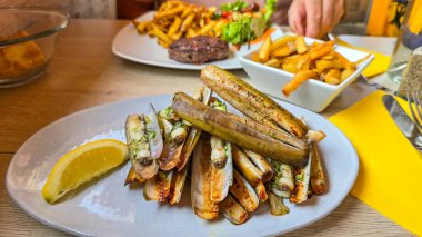 Kızarmış deniz kabuğu, sarımsaklı jilet, maydanoz ve bir dilim limon. Yakınlarda kızarmış patates var.