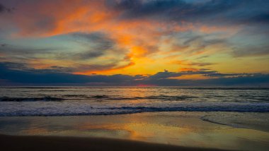Gün batımında ya da gün doğumunda okyanus kıyısında romantik bir akşam. Güneş ışığı su yüzeyine, turuncu bulutlara ve ıslak kuma yansıyor..