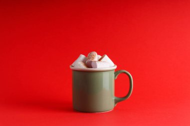 Yeşil kupa dolusu sıcak çikolata ve marşmelov izole edilmiş kırmızı arka plan, yeni yıl ve noel teması