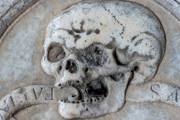 Close-up on human skull with an open mouth carved in a marble wall