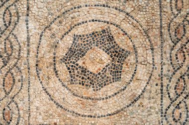 Eski dekoratif mozaiğe yakın çekim. Çemberlerin içinde karmaşık motiflerle çevrili soyut bir sembol gösteriyor.