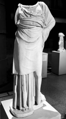 Siyah ve beyaz, başsız antik mermer kadın heykeli tunik içinde poz veriyor.