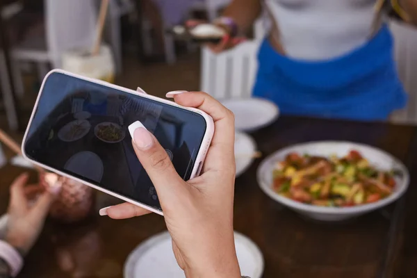 Cep telefonlu bir kız yazın her restoranda yemek fotoğrafı çekiyor.