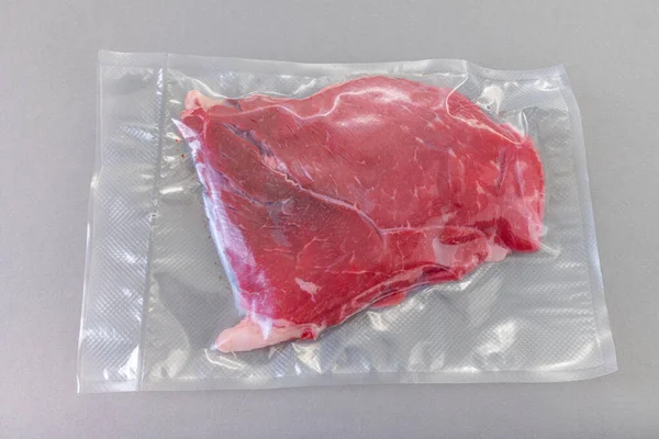 Raw beef steak in vacuum-sealed package for sous vide cooking on gray background