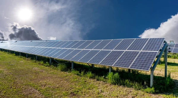 Solar Panels in green field in country on blue sky with sun shining, Photovoltaic solar cells energy farm for production of clean renewable energy from the sun\'s rays, copy space
