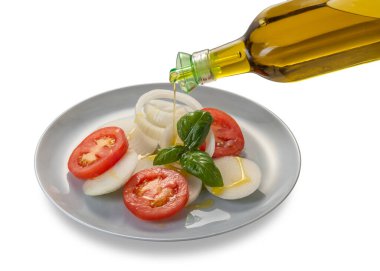 Beyaz soğan halkalı domates salatası ve cam şişeden dökülen zeytinyağlı fesleğen yaprakları ve kırpma yolu da dahil olmak üzere beyaz tabaktaki damlalı koruyuculu kapak.