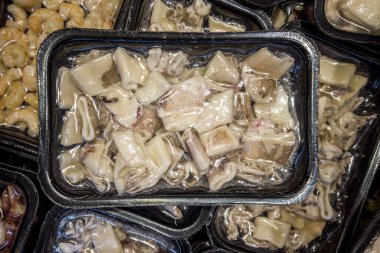 Süpermarketteki soğutucu tezgahlarda satılmak üzere vakumlu vide pişirme tepsilerinde önceden pişirilmiş kalamar.