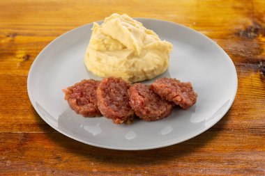 Ahşap masa üzerinde patates püresi ve adaçayı yapraklı pişmiş sosisli cotechino dilimleri. Plaka kırpma yolu ile kesilmiş