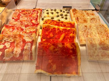 Fırıncı tezgahında satılmak üzere domates soslu, peynirli ve zeytinli kare dilim pizza.