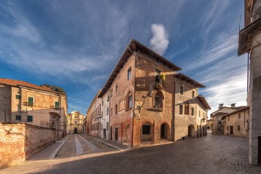 Carignano, Torino, İtalya - 18 Kasım 2023: Via Frichieri ve Via Monte di Pieta arasındaki panorama manzarası Gotik pencereli ve arka planda San Giuseppe kilisesi bulunan ortaçağ kökenli bir ev