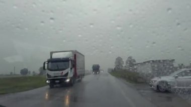 Yağmurda araba ve kamyonların olduğu yol hareket eden sileceklerle araba kristalinden sübjektif görüş