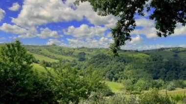İtalya 'daki UNESCO Dünya Mirası Bölgesi olan Langhe' deki Serralunga di Alba çevresinde mavi gökyüzü ve beyaz bulutlu üzüm bağları ve ormanları olan tepelerin manzarası tipik bir Barolo şarap bölgesi..
