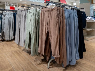 Giysi mağazasında satılık çamaşır ipinde çeşitli renklerde bez pantolonlar sergileniyor.