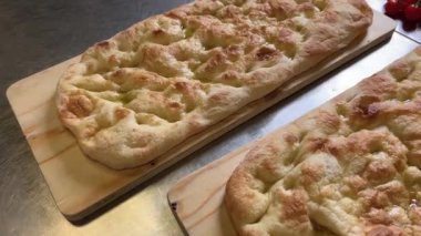 Ekstra saf zeytinyağlı Focaccia ahşap doğrama tahtasında, tipik Cenova düz ekmeği veya pinsa romana veya schiacciata toscana, üst görüş açısında kayar.