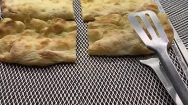 Satılık paslanmaz çelik maşayla sergilenen Focaccia ekmeği dilimleri, Genova zeytinyağlı düz ekmeğin üzerinde kaydırma.