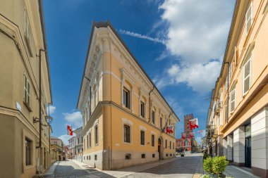 Asti, Italy - August 20, 2024: Historic buildings in Corso Vittorio Alfieri and Via Ottollenghi cobblestone pedestrian area with a view of the Comentina tower and the banners of the Palio di Asti clipart