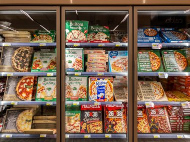 İtalya - 24 Temmuz 2024: İtalyan süpermarketlerinde satılmak üzere soğutulmuş vitrinde sergilenen farklı marka paketlerde çeşitli marka ve aromalı dondurulmuş hazır pizzalar