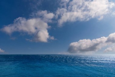 Mavi gökyüzü üzerinde deniz manzaralı, beyaz bulutlu, güneş yansımalı bir deniz manzarası. Fransa 'nın Korsika Adası' ndan görülen Akdeniz manzarası