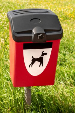 Yeşil çayırdaki köpek dışkısı öğütücüsü için kırmızı çöp kutusu. Köpek kakası için köpek resmi olan park kutusu.
