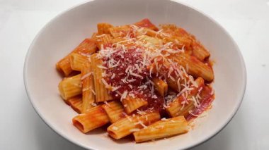 Izgara parmesan peyniri beyaz tabakta domates soslu makarna üzerine dökülüyor.