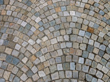 Vantilatör şekilli kaldırım taşlarının dokusuyla döşenmiş bir sokakta farklı renkte kübik taşlar.