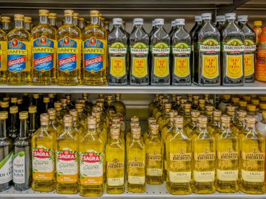 İtalya - 5 Ağustos 2025: İtalyan bir süpermarkette raflarda sergilenen cam şişelerde çeşitli markalardan oluşan zeytinyağı.