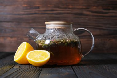Koyu çay ve limonlu çaydanlık ahşap bir masada. Kırsal zemin sıcak, samimi bir ortam ekler, doğal içecekleri sergilemek ya da limonu gevşetmek için ideal hale getirir.