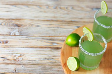 Limonlu Margarita 'nın tepeden görünüşü, tuz kenarlı, limon dilimiyle süslenmiş, tahta bir tahtanın üzerine, taze limonların yanına yerleştirilmiş. Yaz içkileri, kokteyl partileri ve ferahlatıcı hisler için ideal..
