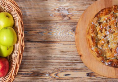 Hasır bir sepet elma ve ahşap bir masada pudra şekerli kafes elmalı turta. Ev yapımı yemek temaları için rahat, kırsal bir sonbahar sahnesi..