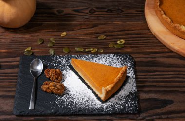  Koyu bir tabakta ev yapımı kabak turtası, pudra şekeri, ceviz ve kabak çekirdeği ile süslenmiş. Kırsal ahşap arka planda mükemmel sonbahar tatlısı..