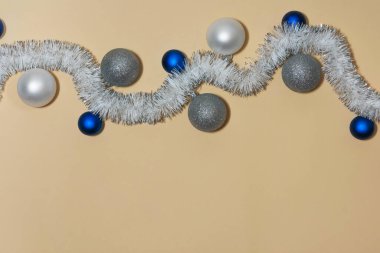 Bej arka planda mavi ve gümüş renkli Noel topları olan beyaz bir çelenk. Tatil dekorasyonu, şenlikli tasarımlar ve mevsimlik projeler için mükemmel..