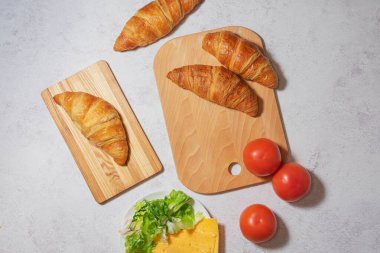 Çıtır kruvasan taze domates, marul ve peynirle beyaz arka planda güzelce yerleştirilmiş. Mutfak, yemek tarifi veya fırın sunumları için ideal.