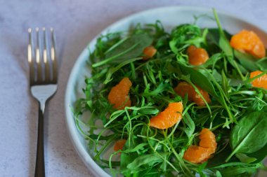Yeşil yapraklı ve mandalinalı taze salatanın yakın plan görüntüsü, malzemelerin canlı renklerini ve dokularını vurguluyor..