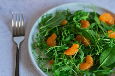 Close-up view of a fresh salad with green leaves and mandarin segments, highlighting the vibrant colors and textures of the ingredients. clipart