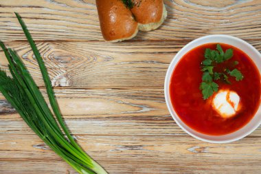 Bir kase yeşil soğan ve dereotla süslenmiş ekşi krema ve ahşap bir masada iki rulo ekmek..