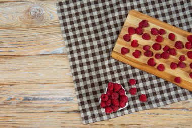 Kırsal ahşap bir masada kalp şeklinde bir kasede damalı kumaşla taze ahududular. Üst manzara, canlı renkler, rahat mutfak havası..
