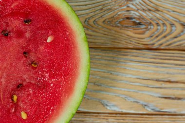 Ağaç desenli bir yüzeyde sulu bir karpuz diliminin yakın çekimi. Parlak kırmızı et ve yeşil kabuk tazeliği, yaz havasını ve sağlıklı atıştırmalıkları çağrıştırıyor..