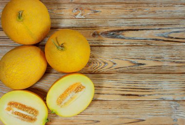 Bir grup olgun sarı kavun, görülebilir çekirdekli yarı yarıya da dahil, kırsal ahşap üzerine yerleştirilmiş. Tazelik, yaz hasadı ve sağlıklı beslenmeyi çağrıştırıyor..