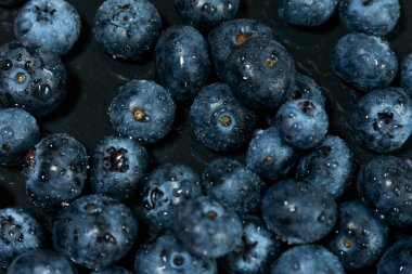 Koyu dokulu yüzeyde su damlacıkları olan taze yaban mersinlerine yakın çekim. Koyu mavi renkler ve doğal detay beslenme, tazelik ve yaz üretimini çağrıştırır.