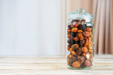 Kayısı, kuru üzüm ve incir gibi karışık meyvelerle dolu cam kavanoz kırsal ahşap masa. Yumuşak perde arkası olan rahat mutfak ortamında sağlıklı atıştırmalık depolama.