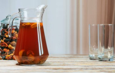 Kayısı ve böğürtlenli ev yapımı bir sürahi ev yapımı meyve kompostosu, bir kavanoz kurutulmuş meyve ve kırsal ahşap masada boş bardakların yanında. Hafif rahat arkaplan