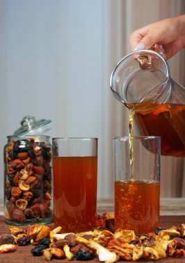 Elle kurutulmuş meyveyi bardaklara doldurur. Biri doldur, biri doldur. Kavanozda kurutulmuş meyve ve kırsal yüzeye saçılmış parçalar. Doğal ev yapımı içecek sahnesi.