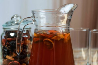 Bir sürahi ev yapımı kurutulmuş meyve kompostosu yüzen dilimler, bir kavanoz kurutulmuş meyve ve boş bardaklar kırsal masada. Mutfak ortamında doğal içecek.