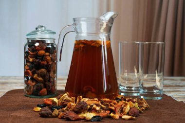 Dağılmış meyve, kavanoz ve kırsal masada boş bardaklarla dolu bir sürahi kurutulmuş meyve ezmesi. Doğal malzemeli ve yumuşak arkaplanlı ev yapımı içecek sahnesi