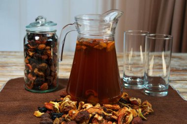 Bir sürahi ev yapımı kurutulmuş meyve kompostosu dağınık meyve, kavanoz ve boş bardaklar kırsal ahşap masa üzerinde. Tarafsız arka planı olan rahat mutfak sahnesi