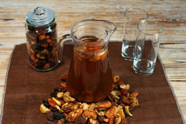 Bir sürahi ev yapımı kurutulmuş meyve kompostosu dağınık meyve, kavanoz ve boş bardaklar kırsal ahşap masa üzerinde. Mutfak ortamında doğal içecek.