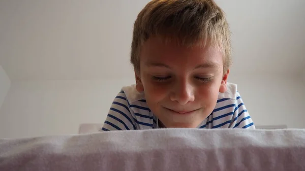 可爱的小高加索男孩10岁躺在卧室的床上 狡诈地微笑着 斜视着 闭上眼睛 期待一个惊喜 一个玩笑和宠爱 Peekaboo 玩百叶窗 — 图库照片