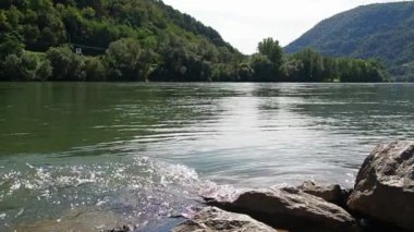 Nehrin dalgaları kayalık sahilde buluşur. Yeşil uçurumdaki su girdabı. Güneş parlıyor. Zvornik, Bosna-Hersek. Drina Nehri Bankası, ağır çekim. Su hareketi